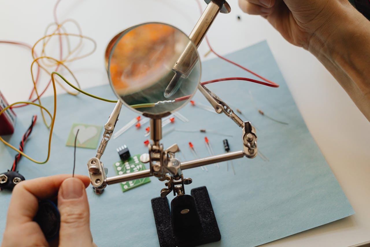Detailed view of a soldering process on a workbench, using a magnifying glass for precision.